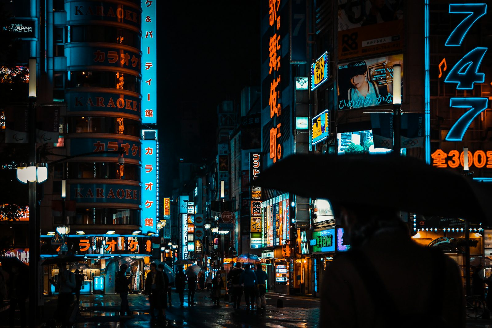 A wet street at night under neon signs and umbrellas